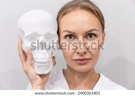 Rhinoplasty. Portrait of adult Caucasian woman holds cranium near face. Concept of plastic surgery and professional cosmetology.
