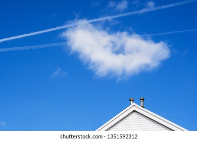 Rhondda, UK / 24th March 2019 : White Roof Gable Or Pine End Of House With White Fluffy Cloud On Blue Sky And Airplane Vapour Trails.