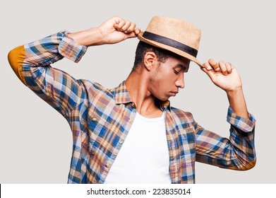 In the rhythm of my life. Handsome young Afro-American hipster holding hands on his hat while standing against grey background