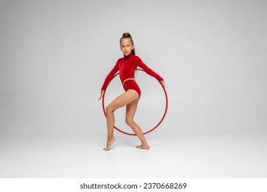 Rhythmic gymnastics. Gymnast child performs an exercise with hoop on white background in an red swimsuit. Children's professional sports. Copy space - Powered by Shutterstock