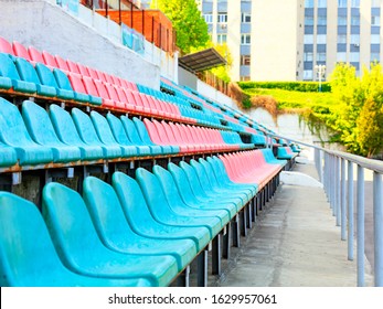 The rhythmic rows of empty turquoise and red plastic chairs of an old sports stadium against the background of sunlight in the background.