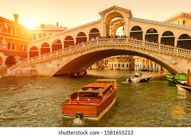 Rialto Bridge over the Grand Canal at sunset, Venice, Italy. It is a famous landmark of Venice. Boats sail under the Ponte di Rialto in summer evening. Sunny nice view of old architecture of Venice.