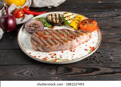 Rib Eye Steak With Grilled Vegetables. A Classic Hot Dish Of Premium Beef Steak (cowboy Ribeye Or Entrecote) With Eggplant, Zucchini, Peppers, Tomatoes And Onions On A Wooden Kitchen Table.