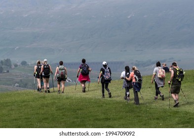 Ribblesdale, North Yorkshire, England - June 13 2021: Hillwalking group on three peaks path sharply focused against softly focused, heat hazy backdrop of Whernside hill and Ribblehead viaduct.