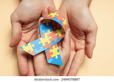 Ribbon with colorful puzzle pieces in hands on light background. World autism day concept - Powered by Shutterstock