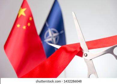 Ribbon Cutting Ceremony. Scissors Cut Red Ribbon. 
China And NATO Flag Bluered On The Background. Start Of A Partnership Concept