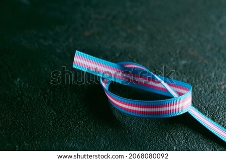 a ribbon patterned with the transgender pride flag on a dark gray textured surface