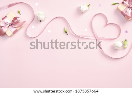 Ribbon in shape of heart with gift boxes and rose flowers on pink background. Happy Valentines day, Mothers day, birthday concept. Romantic flat lay composition. 