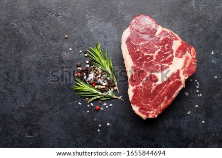 Ribeye fresh raw beef steak with spices on stone board. Top view flat lay with copy space
