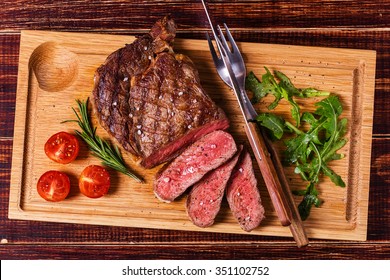 Ribeye Steak With Arugula And Tomatoes On Dark Wooden Background.