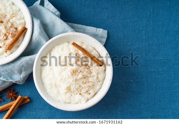 Rice pudding. French milk rice
dessert. Healthy Vegan diet breakfast with coconut milk, cinnamon.
Blue linen textile. Dark background. Top view, copy
space