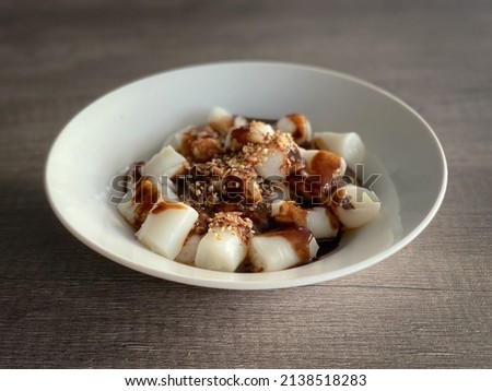 Rice rolls or zhu chang fen or chee cheong fun drizzled in black sauce and sprinkled with fried onions on top. Laid in white porcelain plate and put on wooden grain background. Selective focus.