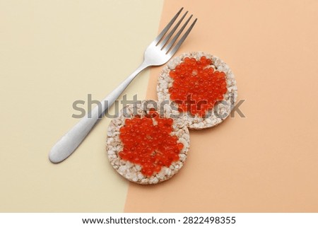 Rice round bread with red caviar and fork on beige background