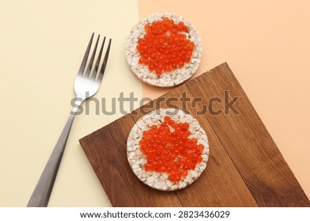 Rice round bread with red caviar and fork on beige background