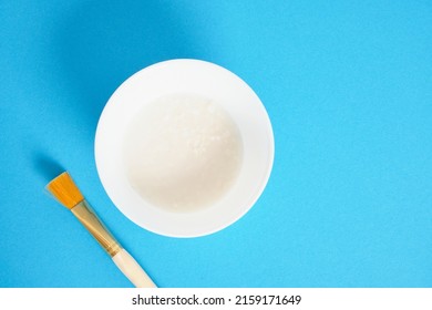 Rice Water And Cosmetic Brush On Blue Background, Natural Homemade Face And Hair Care Fermented Cosmetic