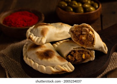 Rich Argentine empanadas in a still-life environment, wooden background, with olives, pepper and paprika. Kitchen concept - Shutterstock ID 2005234037