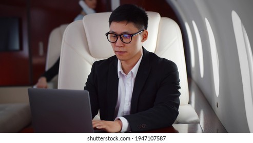 Rich Asian Businessman Flying First Class And Working On Plane With Laptop. Portrait Of Korean Billionaire Using Computer Travelling In Private Jet