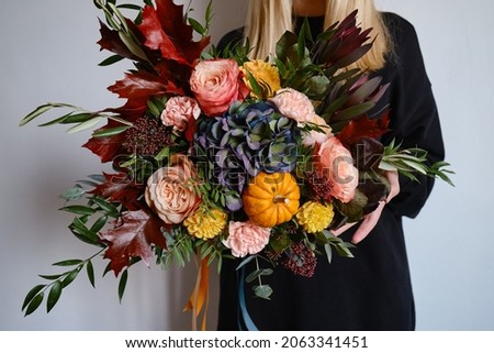 Rich bouquet with autumn flowers and a pumpkin in the hands of a girl on a light background. Bright festive bouquet. A holiday gift. Beautiful autumn flowers. Florist girl collected a bouquet