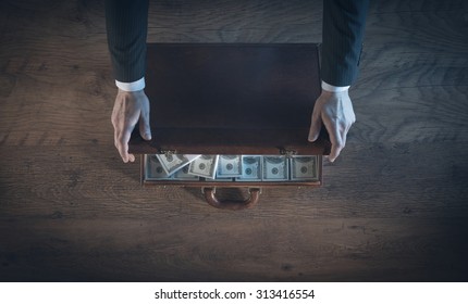 Rich businessman opening a leather briefcase filled with dollar packs, top view, unrecognizable person