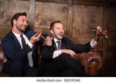 Rich businessmen making self photos while sitting on sofa in restaurant. Handsome rich men with cigars smiling for camera.