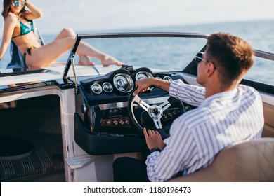 Rich Caucasian Businessman In Trendy Shirt And Classy Pants Entertaining Himself With A Pretty Young Hooker In Bikini On His Own Private Yacht, Sailing In Open Sea To Enjoy Sunset.