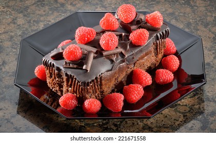 Rich Chocolate Fudge Cake With Raspberries In Black Octagonal Dish.