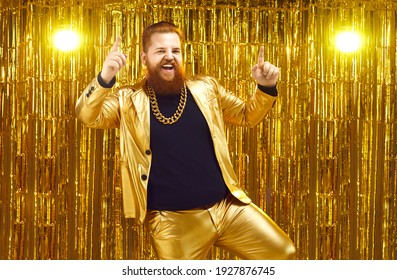 Rich Chubby Man In A Golden Suit Dances At A Party Or Disco On A Bright Shiny Background. Cheerful Unrestrained Red-haired Man With A Massive Chain Around His Neck And Dances And Sings Songs.