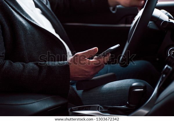 Rich clothes, car\
and mobile device. Working in the car using silver colored\
smartphone. Senior\
businessman.