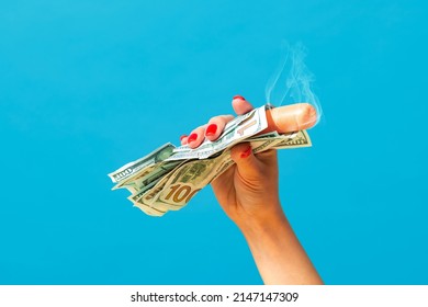 Rich and delicious fast food. Pop art photography.Female hand holding hot sausage wrapped in banknotes isolated on bright blue background. Vintage, retro style, surrealism, minimalism. Complementary