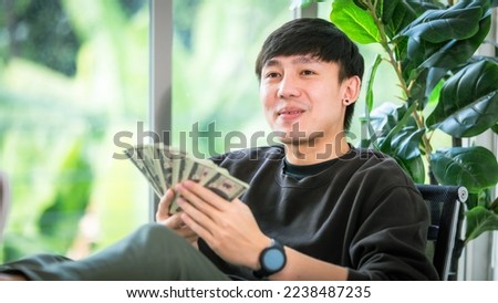 Rich entrepreneur happy to count money in hands earning from successful cash flow growth of business finance while relaxing with smile in company office. Asian magnate man enjoy paying salary award.