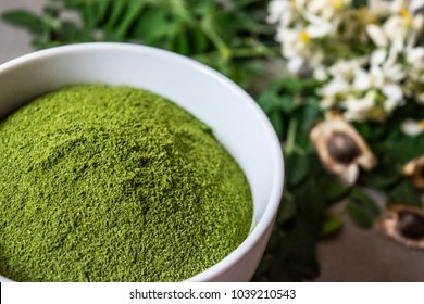 Rich green Moringa powder in white bowl with moringa seeds and fresh moringa leaves side view close up macro 