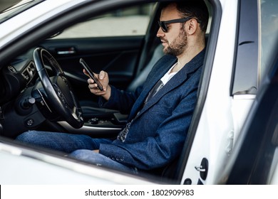 A rich guy looking at his smartphone. Modern car and his owner which using his phone. A foreign car in the street.