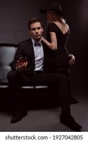 A Rich Handsome Man Drinks Whiskey With A Blonde Mistress In The Evening In Low Light. Photos Of A Couple In Love