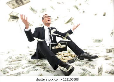 I am rich! Happy young businessman in formalwear throwing money up while sitting near the case full of paper currency