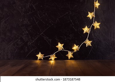 Rich home interior with golden decoration for christmas celebration - glowing lights with stars on black plaster wall and brown wood table, copy space. - Powered by Shutterstock