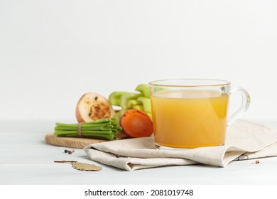 Rich meat or chicken broth with vegetables. In a glass mug, close-up, vegetables in the background.