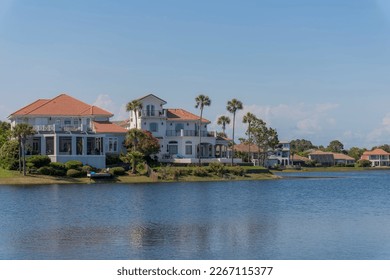 Rich neighborhood with mansions near Four Prong Lake in Destin, Florida. Mansions  villas at the shore of the lake with plants and trees on its yards against the blue sky background.
