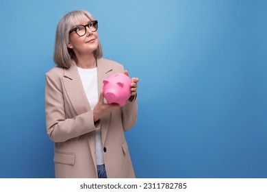 rich old woman with a piggy bank of money on a bright background with copy space - Shutterstock ID 2311782785
