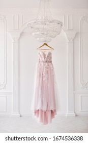 Rich Pink Wedding Dress Hangs On A Chandelier In A White Room