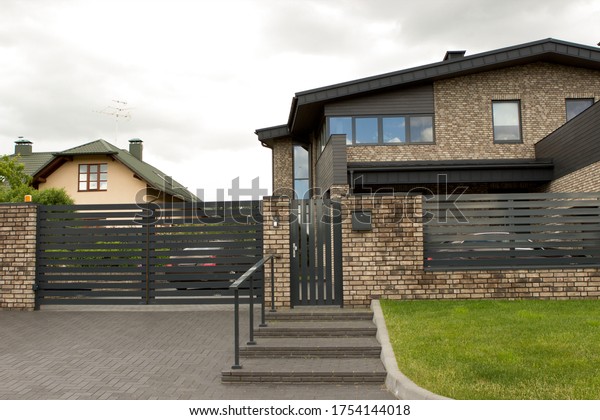 A rich private well-kept\
house with a classic, elegant, simple design. Black roof and fence,\
brick facade, in the courtyard of the car. A suburb of a big\
city.