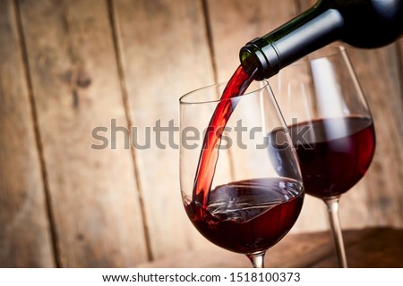 Rich red cabernet wine pouring into a a stylish wineglass from a bottle in a close up tilted angle view over rustic wood Сток-фото © 