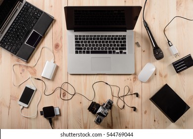 Rich selection of gadgets for easier work. Modern laptops, camera, tablet, power bank, smartphone, computer mouse, charger and black microphone with headphones on the wooden desk.