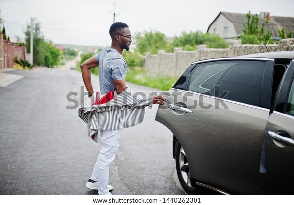 Rich and stylish\
african american man in blazer and white pants, eyeglasses open\
door at his suv car.