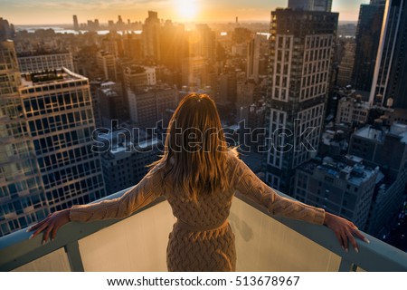 Rich woman enjoying the sunset standing on the balcony at luxury apartments in New York City. Luxury life concept. Successful businesswoman relaxing.