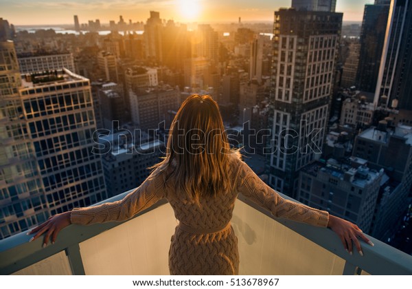 Rich woman enjoying the sunset\
standing on the balcony at luxury apartments in New York City.\
Luxury life concept. Successful businesswoman\
relaxing.