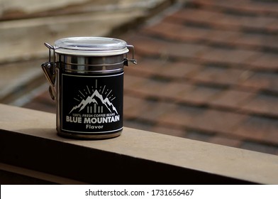 RICHMOND, BC/CANADA- 05/14/2020: Stainless Steel Coffee Can With Latching Plastic Seal Lid, With Blue Mountain Coffee Logo, With Wood Siding And Roof Shingles Blurred Out In The Background. 