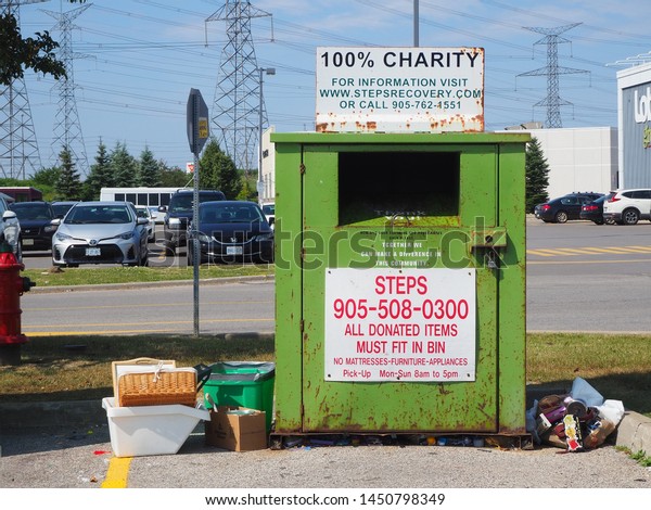 Richmond Hill, Ontario /\
Canada - July 13, 2019: Weathered green donation container with\
thrown garbage.