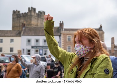 Richmond, North Yorkshire, UK - June 14, 2020: A powerful girl wearing a face mask kneels with her arm raised at a Black Lives Matter protest in Richmond, North Yorkshire