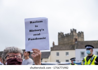 Richmond, North Yorkshire, UK - June 14, 2020: A woman holds an anti-racism placard linking to the COVID-19 pandemic in front of Richmond Castle, North Yorkshire
