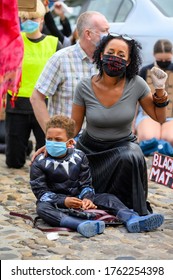 Richmond, North Yorkshire, UK - June 14, 2020: A powerful BAME woman wears a Black Lives Matter PPE Face Mask and salutes while holding her son at a BLM protest